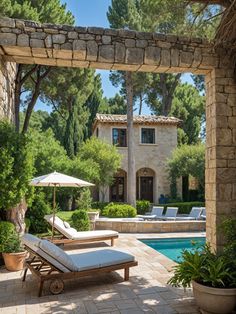 an outdoor pool with chaise lounge chairs and umbrella in front of the house, surrounded by greenery