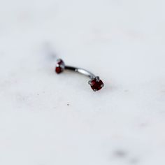 a pair of silver nose rings with red stones on the end, sitting on a white surface