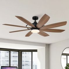 a ceiling fan in a living room with large windows and a television on the wall