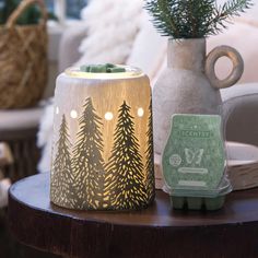 a wooden table topped with a lit candle next to a vase filled with pine trees