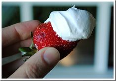 a hand holding a strawberry with whipped cream on it