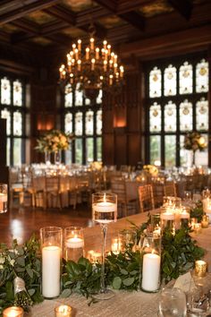 the tables are set with candles and greenery for an elegant wedding reception in front of large windows