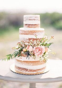 a three tiered cake with flowers and greenery sits on top of a table