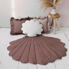 a shell shaped rug on the floor next to pillows and a vase with pamodia in it