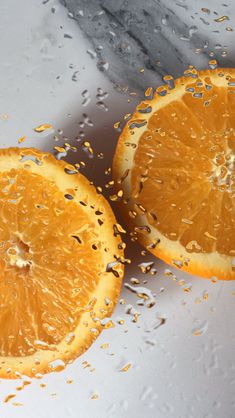 two oranges cut in half sitting on top of a white surface with drops of water