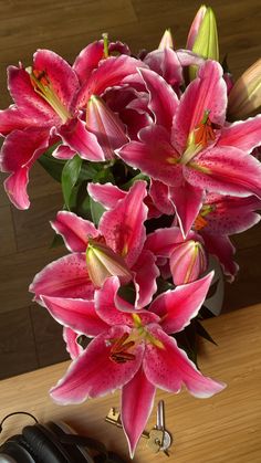 some pink flowers are in a vase on a table with headphones and earbuds