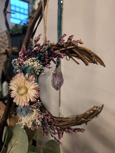 a dried flower wreath hanging from a branch with purple flowers and greenery around it