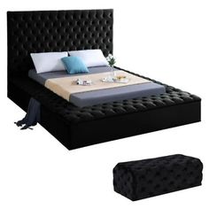 a black bed with white pillows and blue throw pillows on top of it, next to a footstool