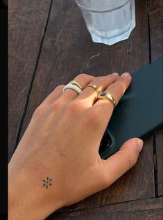 a person's hand holding a cell phone on top of a wooden table next to a glass of water