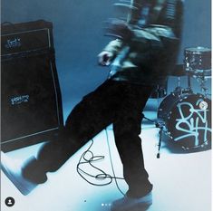 a man standing next to a set of drums on top of a blue floor with graffiti