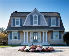 a large house with blue shutters and white trim on the front door is surrounded by flowers