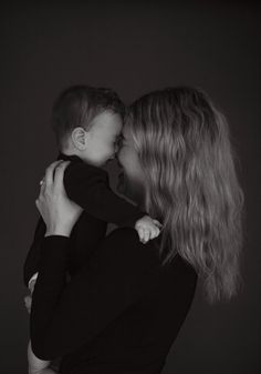 a woman holding a small child in her arms and kissing it's face with both hands