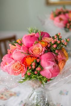 a bouquet of pink and orange flowers sitting on top of a table next to a mirror