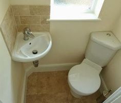 a white toilet sitting next to a sink in a bathroom under a window on top of a tiled floor