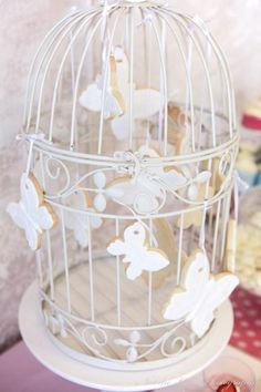 a white birdcage with cookies in it and butterflies on the top is sitting on a table