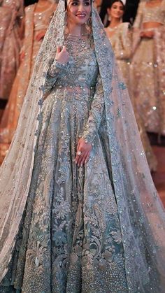 a woman in a blue and white wedding gown standing on the runway with other people behind her