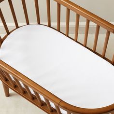 a wooden crib with a white sheet on the top and bottom half, in front of a beige wall