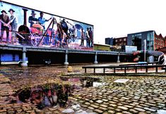 a large mural on the side of a building next to a brick walkway and bridge