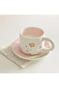 a cup and saucer sitting on top of a pink plate with an open book