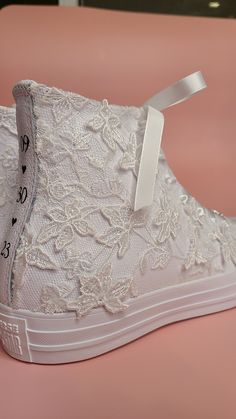 a pair of white lace high top sneakers with bows on the front and side, sitting on a pink surface