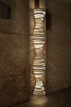 a tall light sculpture sitting in the middle of a room next to a brick wall