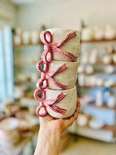 a person holding up a pair of white shoes with pink ribbons on them in a store