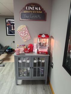 a gray cabinet with popcorn and sodas on top in a room next to a wall