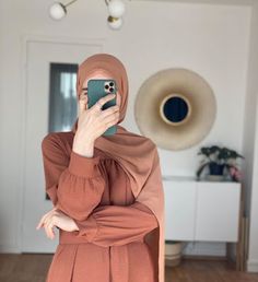 a woman wearing a hijab taking a selfie with her phone in the living room