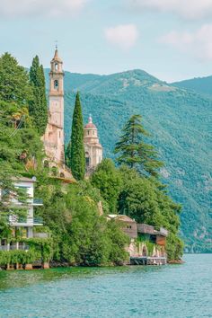 an old church on the side of a hill next to water with trees and mountains in the background