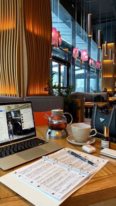 a laptop computer sitting on top of a wooden table next to a cup and saucer