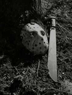 a hockey mask laying on the ground next to a tree with a knife stuck in it