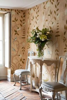 two chairs and a table in front of a wallpapered room with flowers on it