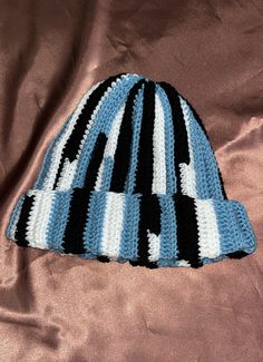 a crocheted blue and black hat laying on a pink satin surface, with the top part of it turned upside down