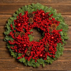 a christmas wreath with red berries and pine cones on a wooden background, top view