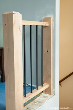 an unfinished wooden railing with black bars on the top and bottom, in front of a blue carpeted floor