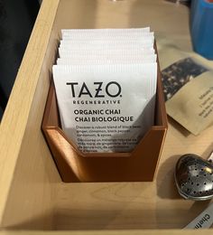 a wooden tray with tea bags in it on top of a table next to a metal strainer