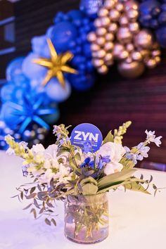 a vase filled with flowers on top of a table next to blue and gold balloons