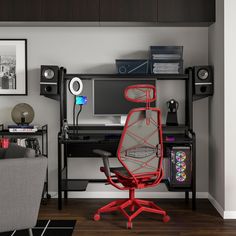 a computer desk with a red chair in front of it and speakers on the wall