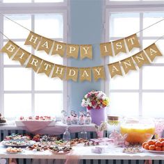 a happy 1st birthday banner hanging over a table filled with desserts and drinks for a party