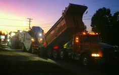 two dump trucks parked next to each other on the side of a road at night