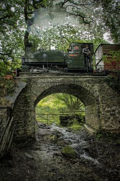 an old train traveling over a bridge in the woods with water running under it and people standing on top