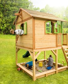 a child's play house in the grass with two children playing on it and an adult