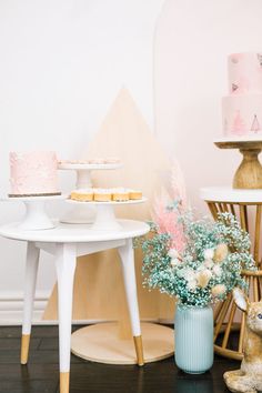 a table topped with cakes and flowers next to a vase filled with pink frosting