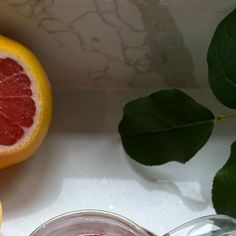 two grapefruits and one orange on a table with some leaves next to it