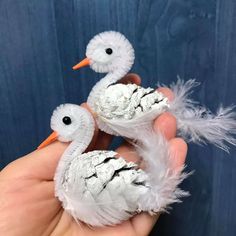 two white birds made out of toilet paper with feathers in their beaks, and one is