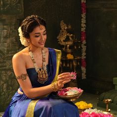 a woman in a blue and gold sari is holding a plate with flowers on it