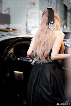 a woman with long blonde hair is getting out of a car wearing a black dress