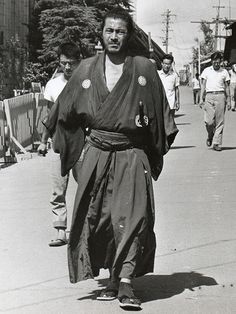 an old photo of a man walking down the street wearing a kimono and carrying something on his back