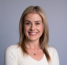 a woman with blonde hair smiling at the camera and wearing a white shirt, standing in front of a gray background