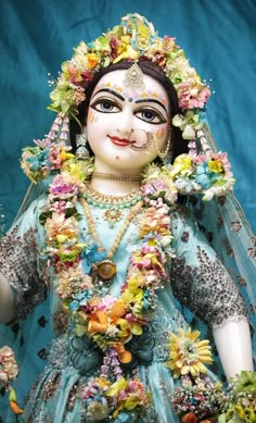 a statue of a woman with flowers on her head and body, dressed in blue